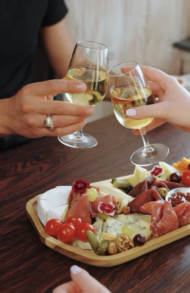 Deux personnes trinquent autour d’une planche de charcuterie et de fromages